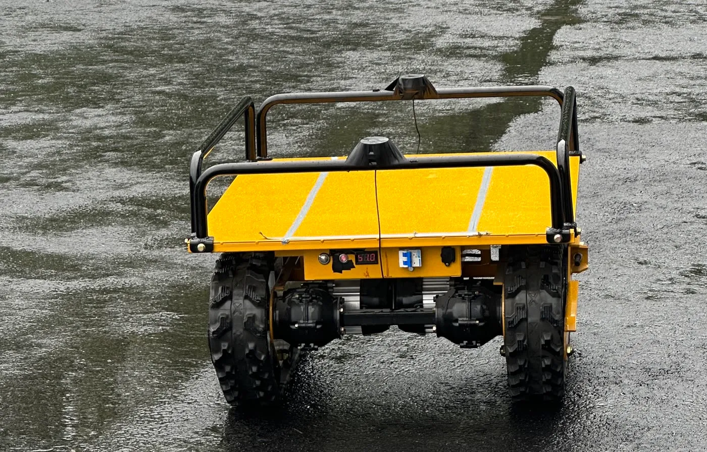 Close view of the tracked UGV's running gear and its roof-mounted GNSS antenna, operating in wet weather.